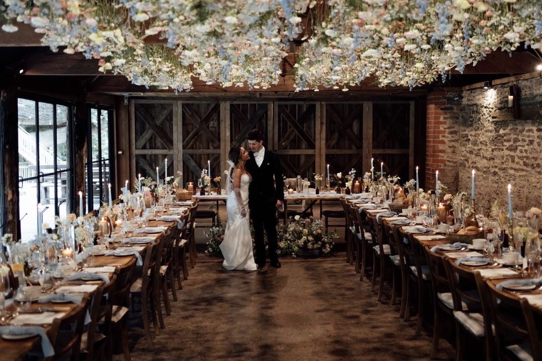 Wedding couple standing in a decorated banquet hall with floral arrangements and candles.