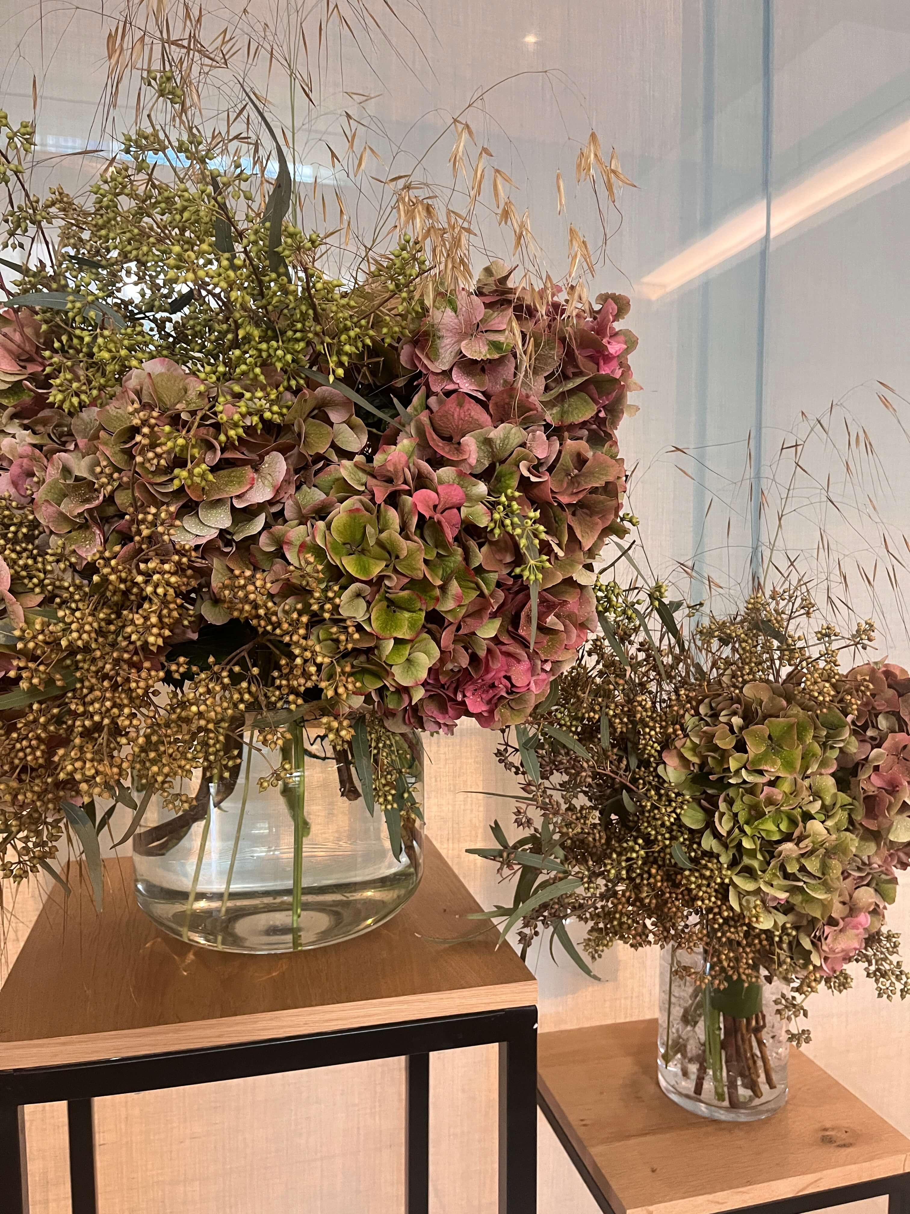 Two glass vases filled with flowers on a wooden surface for a corporate event