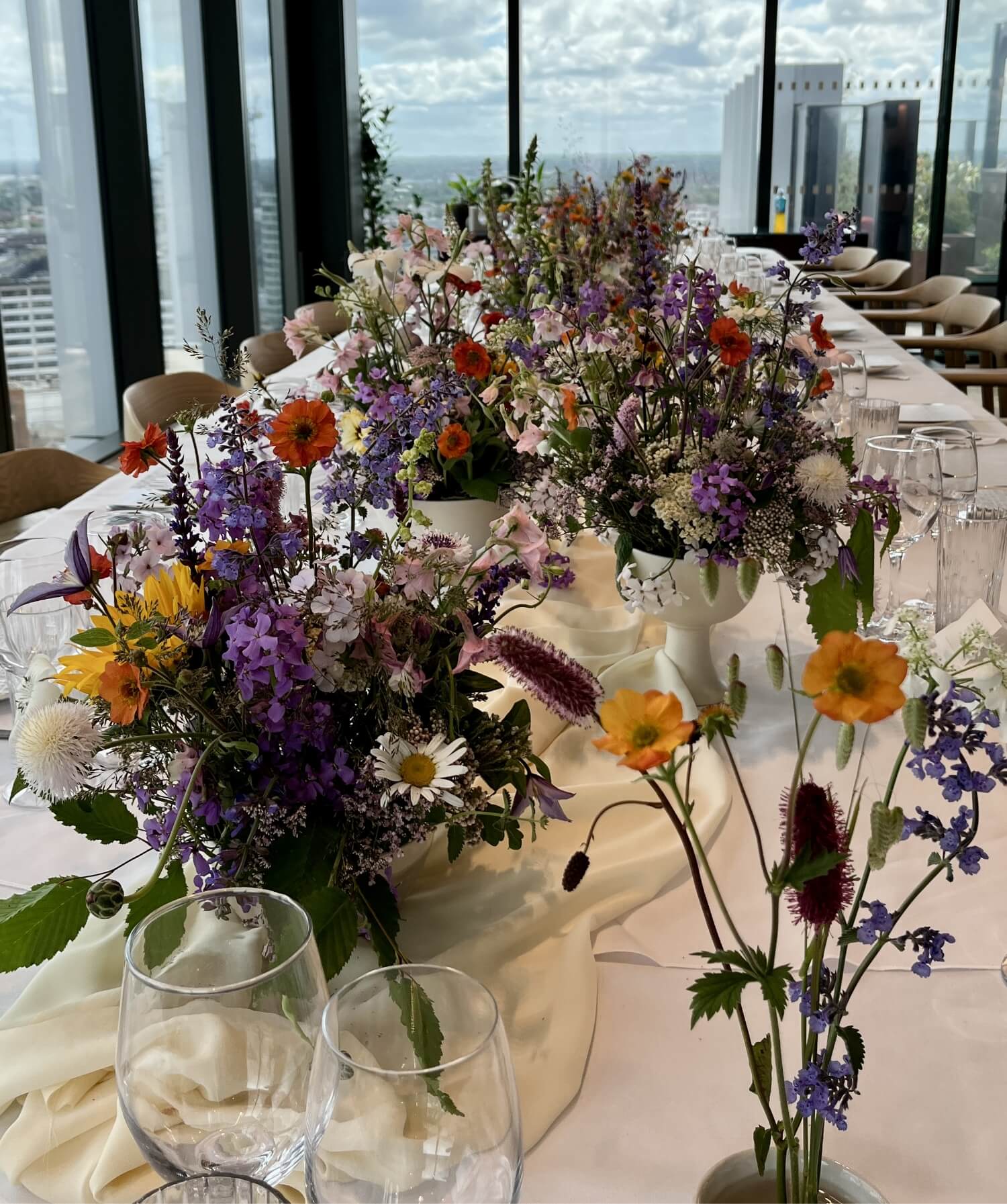 Decorative table setting with flowers and glasses in an indoor setting with a cityscape view.