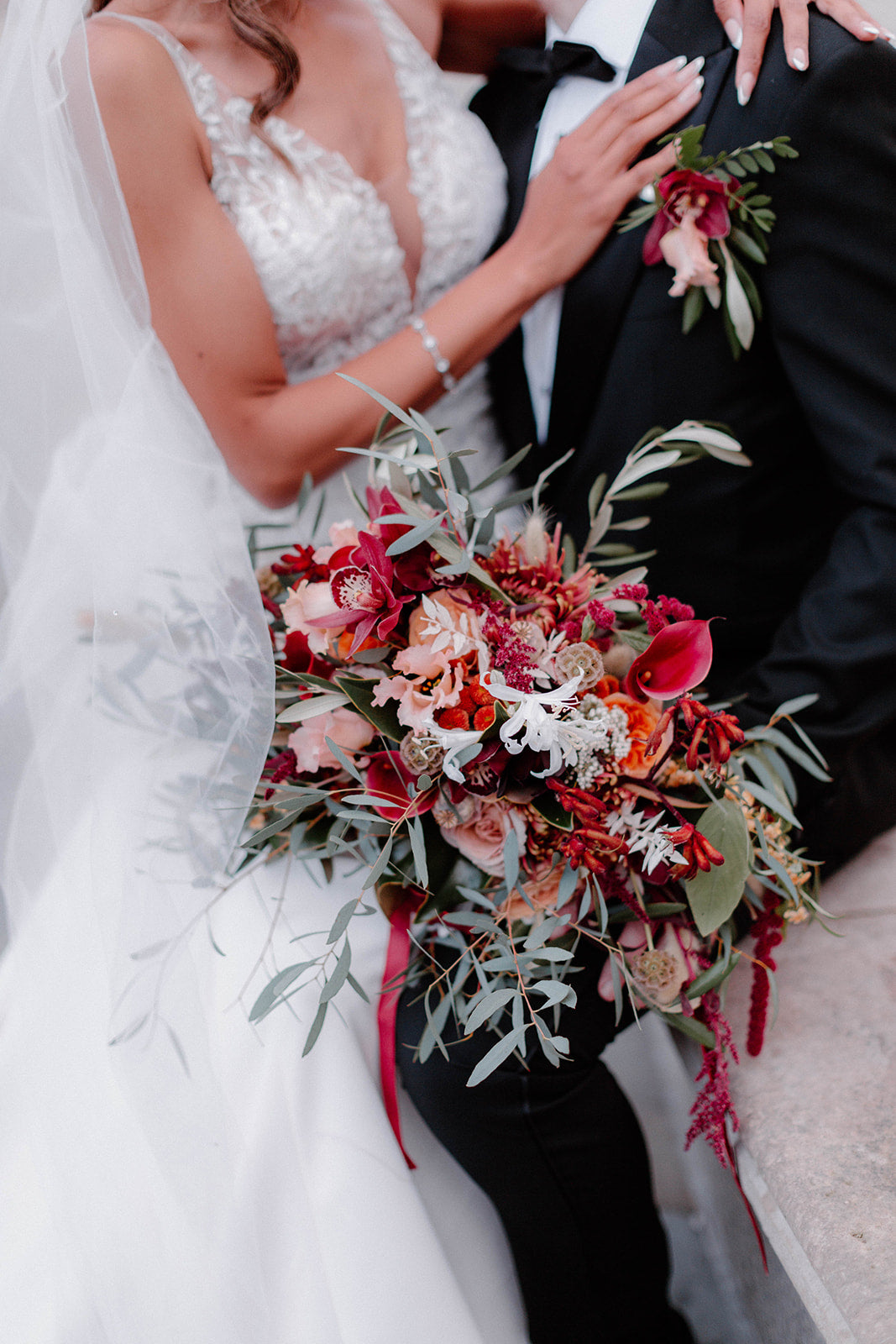 Close up of Bride and groom. The groom is holding a beautiful bouquet of red, white and orange wedding flowers.
